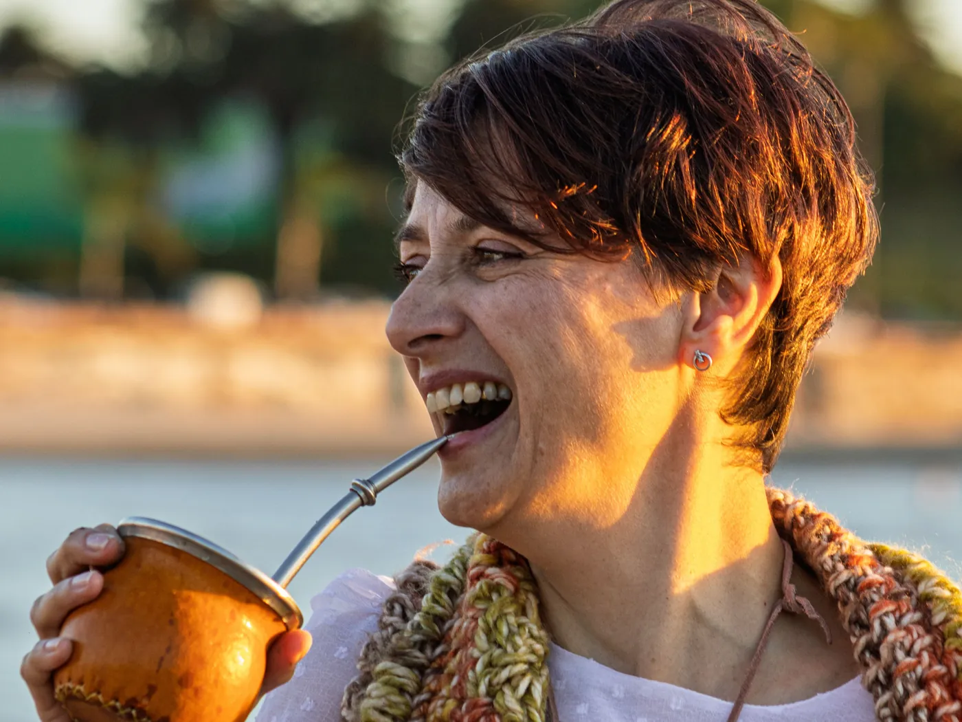 Mujer sonriente tomando mate al aire libre al atardecer